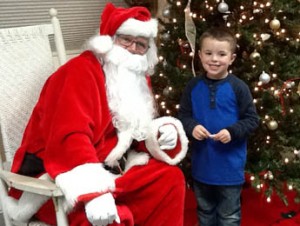 Landen Barrett, 5, the son of Hannah and Matt Barrett of Six Mile, was chosen to light the tree for the town’s annual Old Fashion Christmas last Thursday. Pictured at left, Landen sits with Santa after officially lighting the tree to kick off the Christmas season in Six Mile.